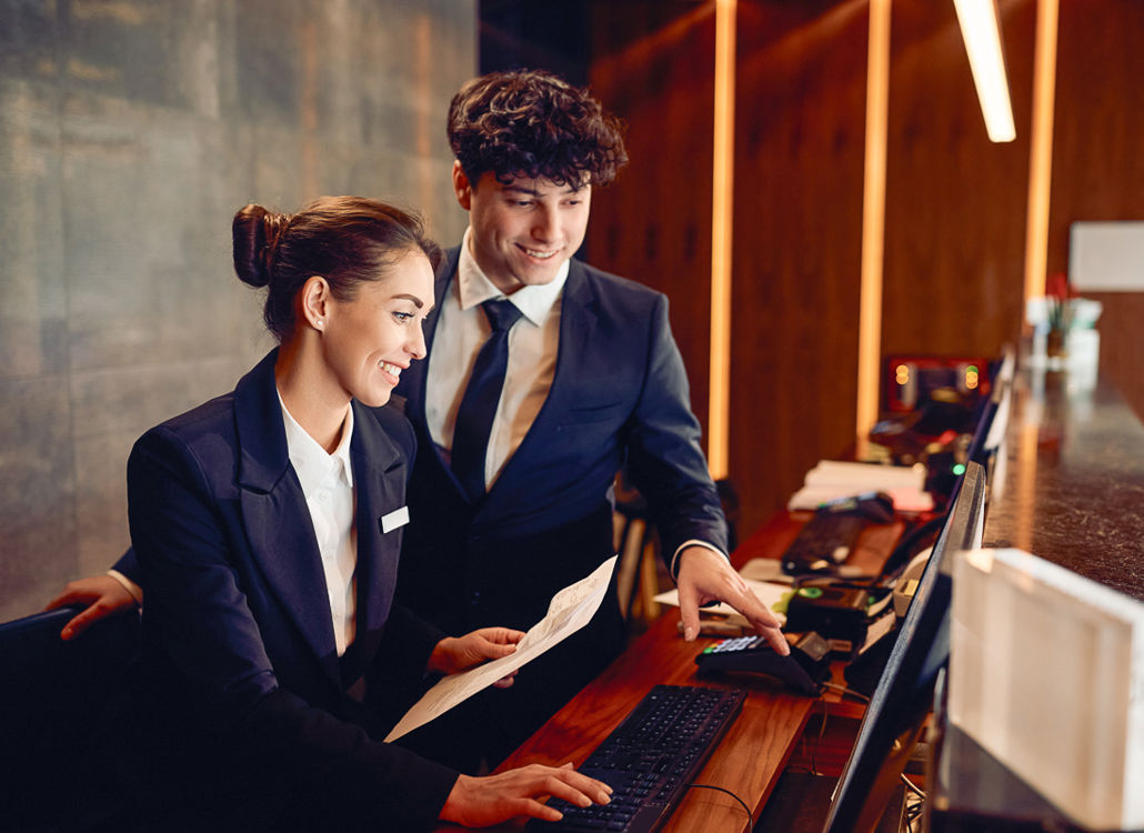 Two hotel receptionists collaborating at a computer, representing teamwork, efficient scheduling, and workforce management
